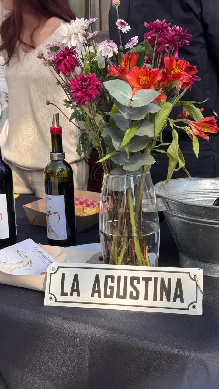 Cartel de La Agustina junto a una botella con la etiqueta del galgo y flores